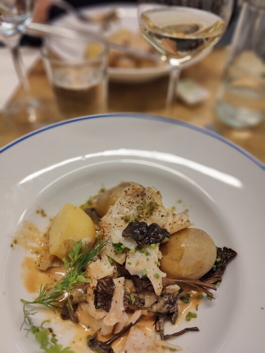 Elegant maträtt med fisk, potatis, svamp, fänkål, serverad på tallrik med vin och suddig bakgrund.