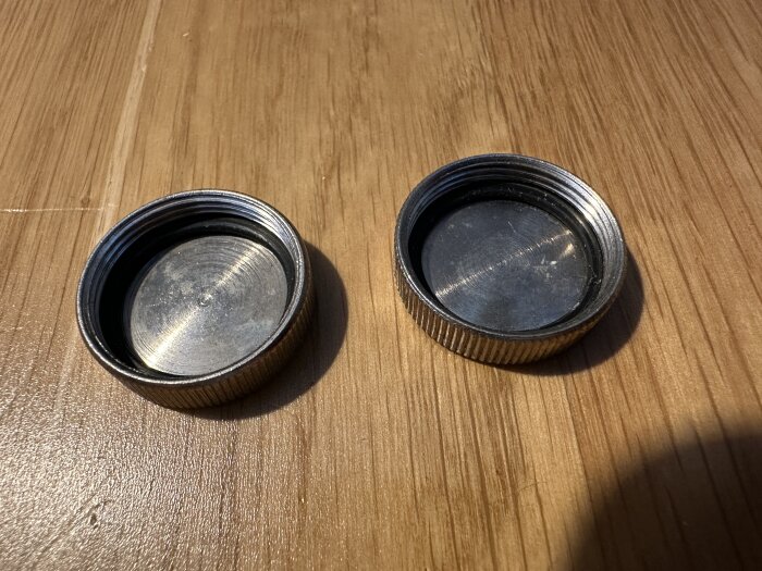 Två svarta metalliska kamerahuslock ligger bredvid varandra på ett träbord.