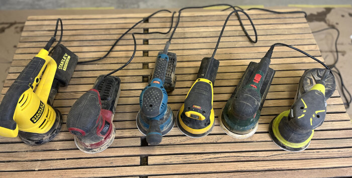 Fem slipmaskiner på träbänk med sladdar. Olika märken och färger, använda verktyg för hantverk.