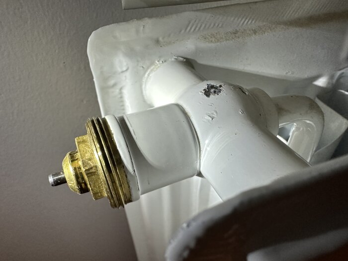 Vit radiatorventil med rost eller smuts, närbild mot grå bakgrund.