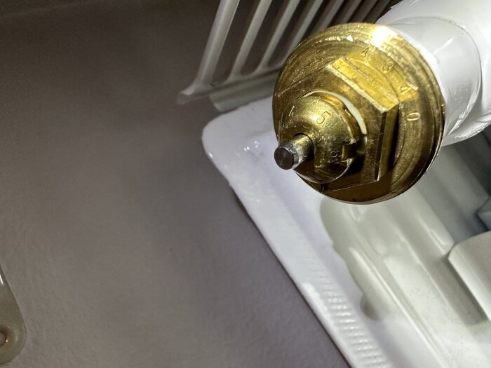 Termoelement av termostatventil på radiator, närbild, regleringsknapp, värmeinställning, vit bakgrund, mässingsdetalj.