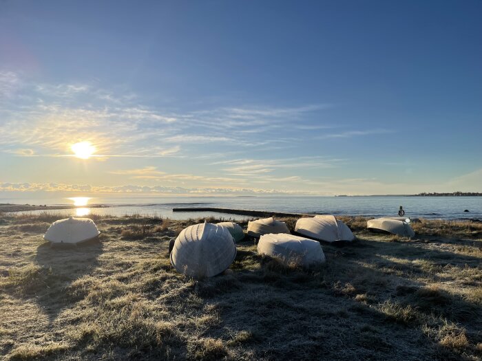 Soluppgång över havet, frostig mark, båtar täckta med presenningar, lugnt, klar himmel.