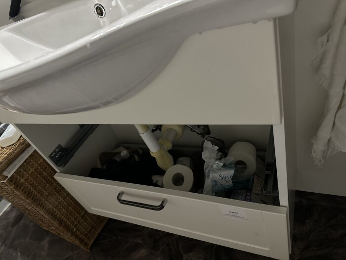 Ett badrumsskåp under en handfat är öppet, visar förvaring av toalettartiklar och städprodukter.