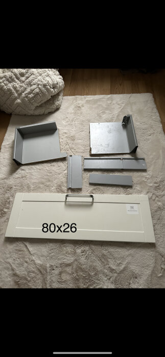 Ihopmontering av möbel, delar på golvet, vit bakgrund, trägolv, vit mysig filt, text "80x26".