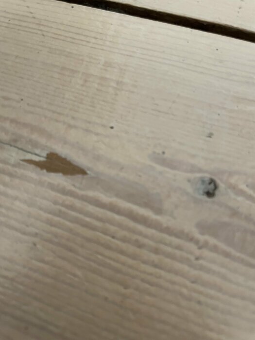 Närbild på ett träyta med skavanker, repor och en flisad del.