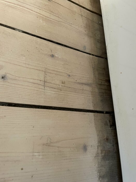 Trägolv med skugga nära vit väggkant, slitage tecken, enkla träplankor.