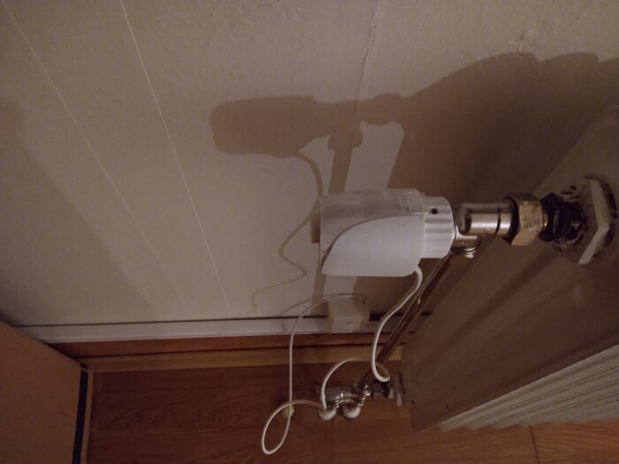 Lampa på vägg med lång skugga på taket, sängkant synlig, bild tagen i sned vinkel.