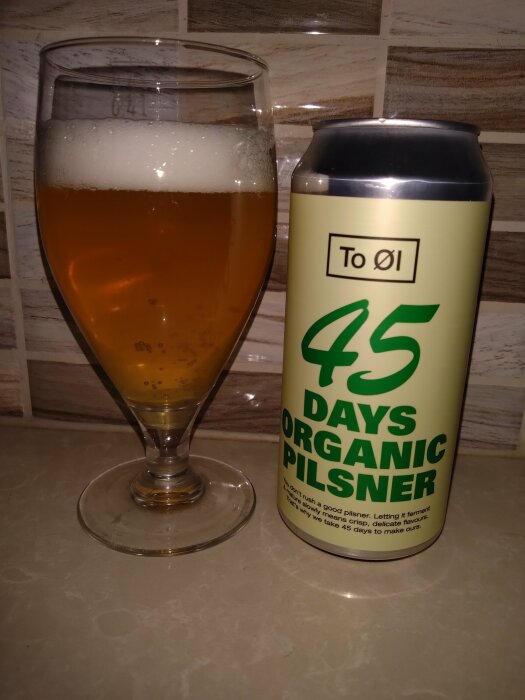 Ett glas med öl bredvid en burk med texten "45 DAYS ORGANIC PILSNER" på en köksbänk.