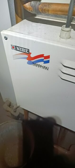 Vit NIBE värmepump eller varmvattenberedare med rostiga rör och etiketten "TAPPMAN". Inomhusmiljö.