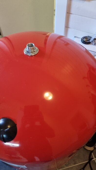 Röd, rund behållare med glänsande yta och metallventil på toppen, möjligen del av ett tryckluftssystem.