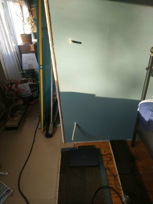 Inomhus, renovering pågår, vägg hälften målad, trägolv, skrivbord, växter i fönster, kablar på golvet.