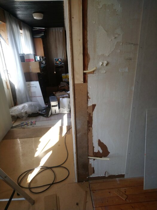 Inredningsrenovering, rörledningar synliga, skadad vägg, mycket röra, ljusinsläpp genom fönster, byggmaterial och verktyg synliga.