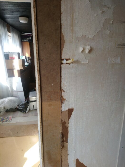 Delvis renoverad vägg med naket hörn, eluttag, sladdar, skadad tapet. Synligt arbetsområde, kartonger och inredning i bakgrunden.