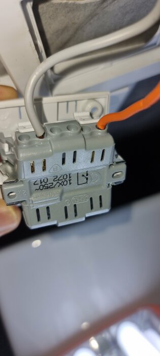 En elektriker installerar en grå kontakt i väggen med vita och orange kablar.