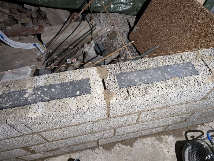 En konstruktionsbild som visar betongblock med armeringsjärn och en verktygsväska; byggnadsarbete och reparationsmiljö.