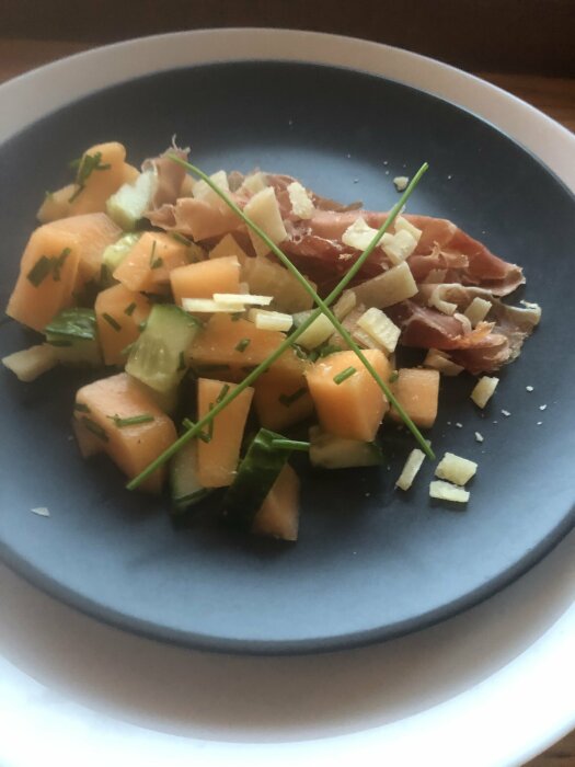 En tallrik med mat: skinka, melon, ost, gröna örter. Färgstark sammansättning. Ljus bakgrund. Fokus i centrum.