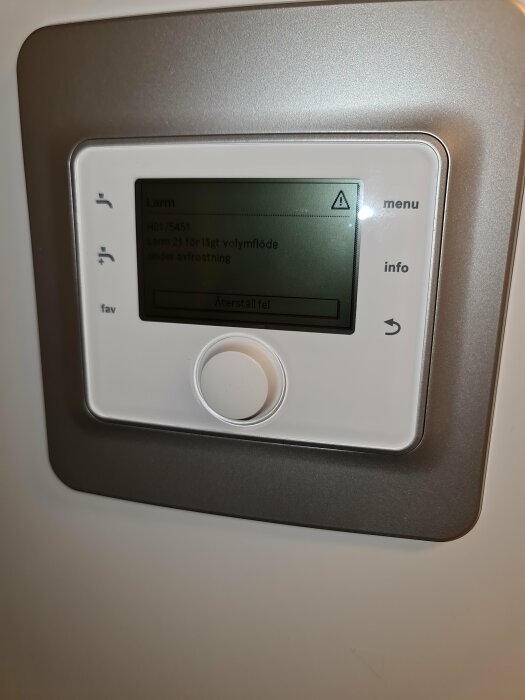 Digital panel visar larm för lågt volymflöde, troligen på en HVAC-enhet, med knappar för navigering och information.