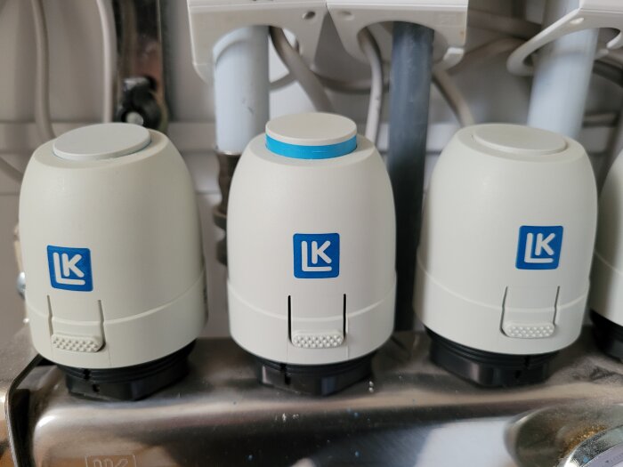 Tre uppochnervända vita plastmuggar med blå detaljer och "LK"-logotyper på ett diskställ.
