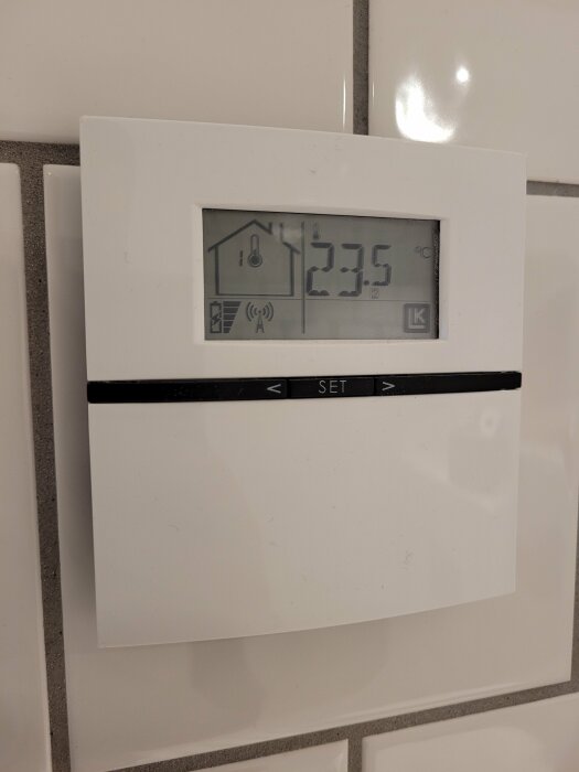 Digital termostat med temperaturvisning på väggen, 23.5 °C, inomhusikoner, ljus bakgrund.