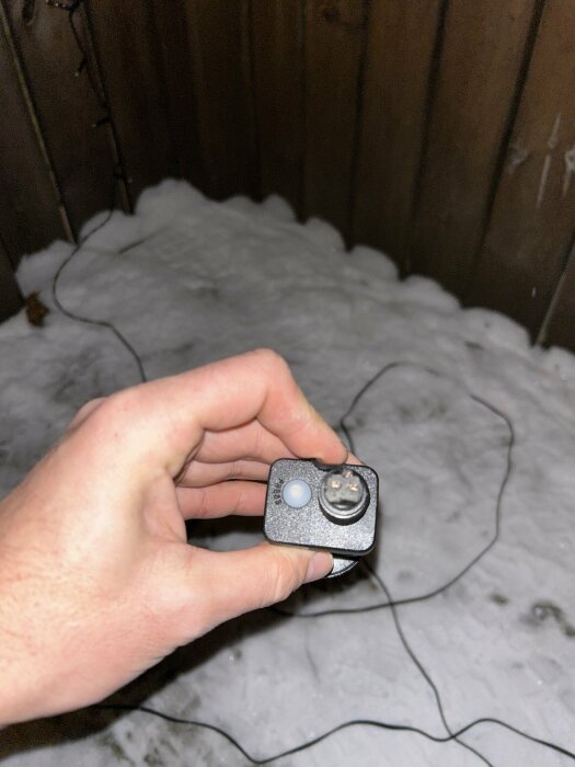 Hand håller en elektronisk enhet med knapp och sladd utomhus vid snö.