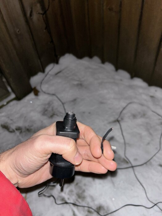 Hand håller avskuren elsladd utomhus mot snötäckt mark och mörkt staket.