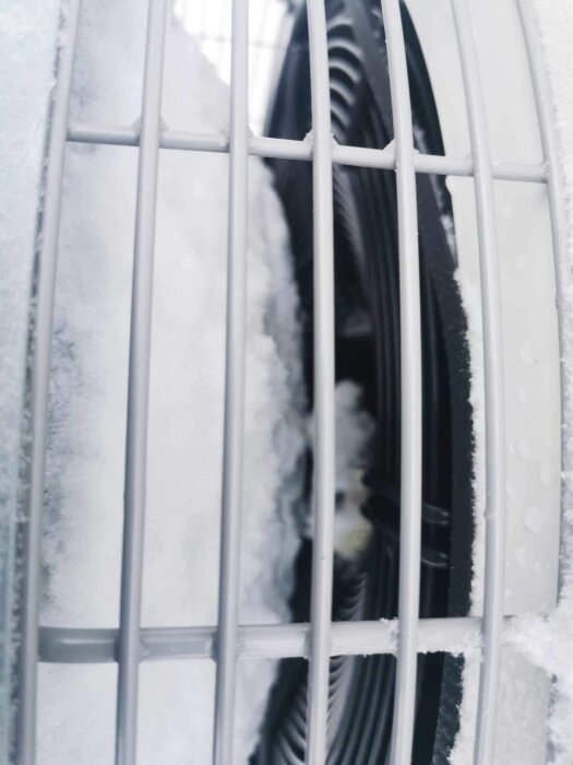 Snötäckt bilfälg synlig genom ett skyddsgaller, kallt och vinterlikt tema.