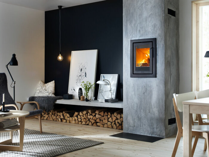 Modernt vardagsrum, kamin, trävedslagring, skandinavisk design, svart accentvägg, konstverk, inbjudande atmosfär.