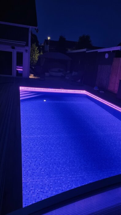 Nattbild av en upplyst pool med blått ljus i en bakgård.