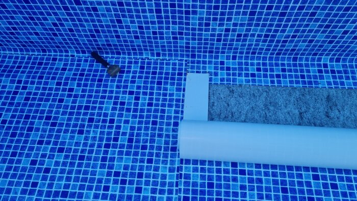 Poolkant med blå mosaikplattor, ledstång, inget vatten, solsken.