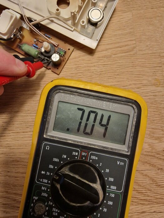 En person mäter elektronikkomponenter med en digital multimeter som visar 7,04 på skärmen.