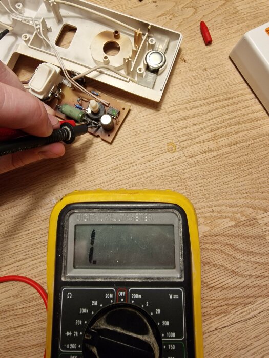 Elektronisk reparation, multimeter används, demonterad apparat, hand, kretskort, komponenter, skruvmejsel, träbord.