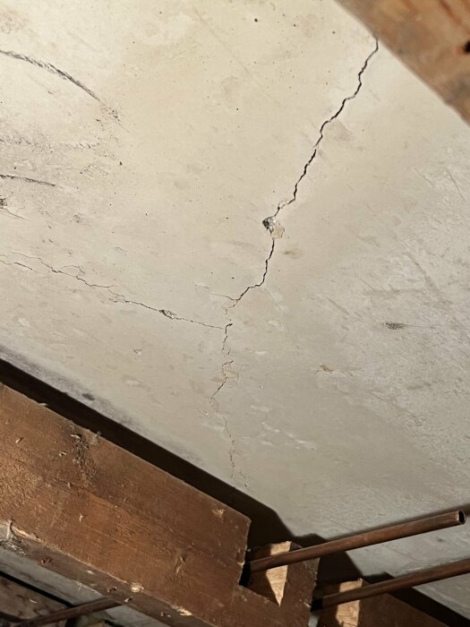 Sprucken betongvägg ovanför brun träbjälkar och rostiga stänger, strukturproblem möjligt, närbild, byggnadsinteriör.