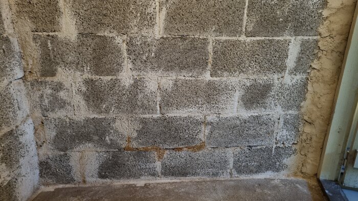 Grå betongmur med spår av fukt och reparationsförsök, inomhus, slitet utseende, osymmetriskt fogarbete.