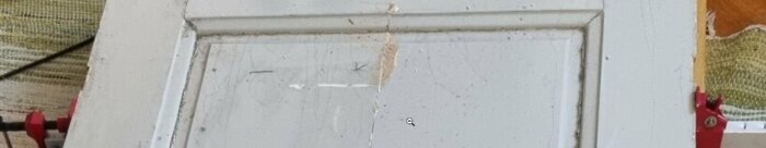 En närbild av en gammal vit dörr med spår av slitage, smuts och skador.