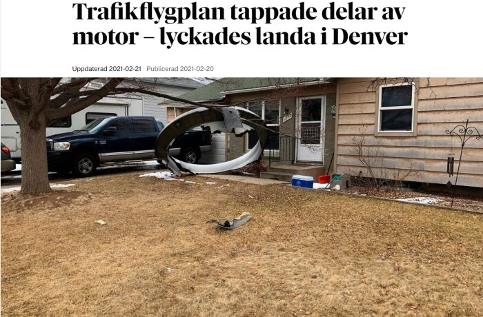 Flygplansdel, sannolikt motorhölje, på husets trädgård, bredvid pickup truck, vinter, ingen person synlig.