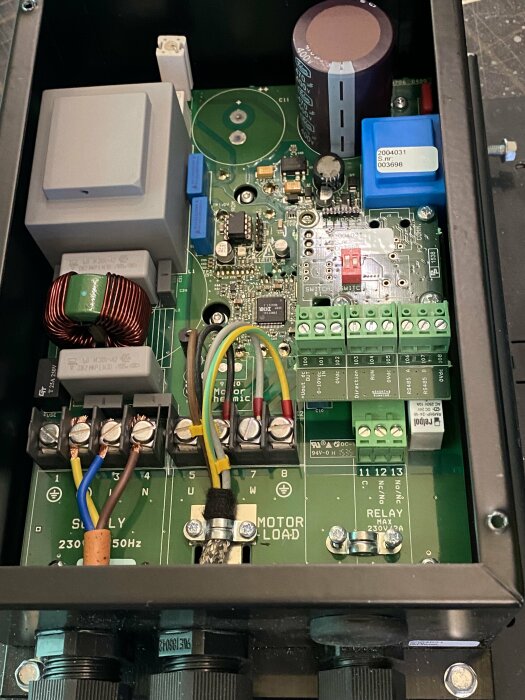 Öppen elektronikbox med kretsar, kondensator, relän och ledningar; komponenter för kraftstyrning eller automation.