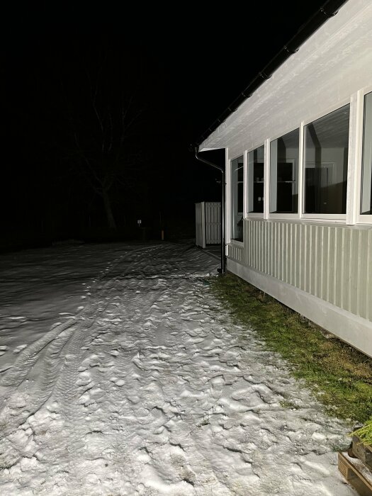 Ett hus på natten med snö på marken och en stark strålkastare som lyser.