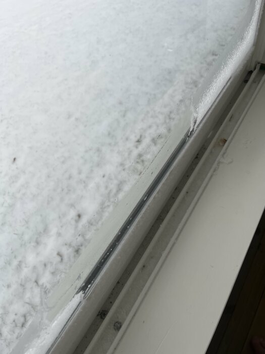Fönsterram med kondens inne och is utanför, vitt karm, otydlig utsikt med snö, indikation på kallt väder.