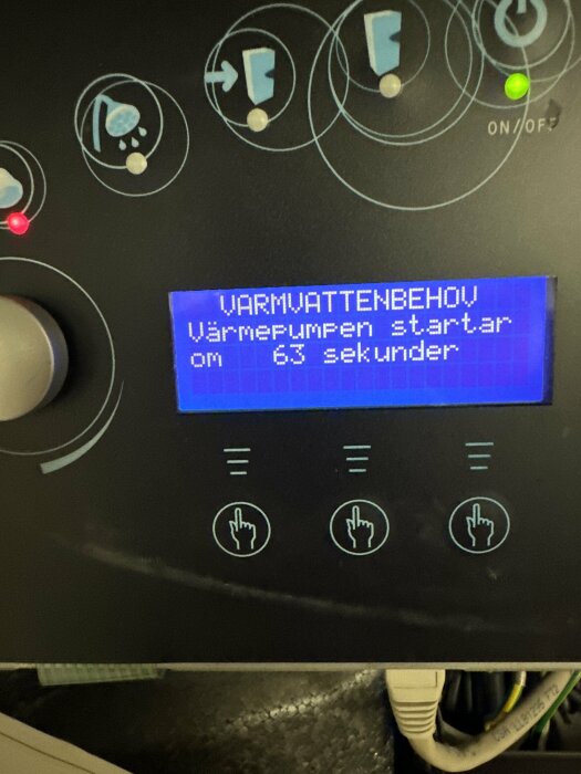 Kontrollpanel för maskin med digital skärm, indikatorlampor och knappsymboler. Text på svenska om värmepumpens start.