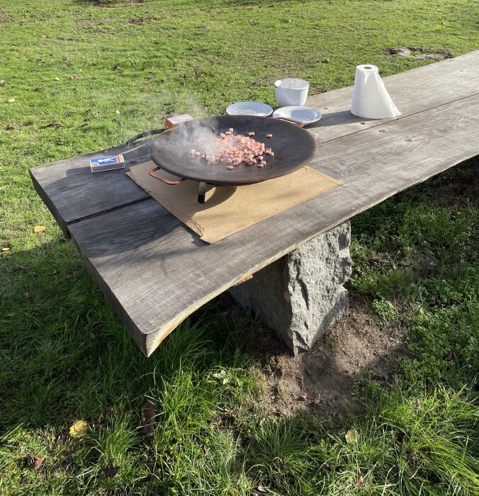 Matlagning utomhus på kadai med tärnat kött, Island flagga, pappershandduk, koppar, gräs och trädgårdsbänk.