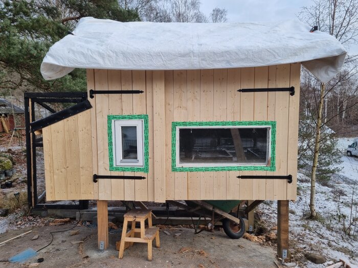 Trähögkiosk på hjul under campingvagnstak, snöig mark, byggs eller renoveras, naturen i bakgrunden.