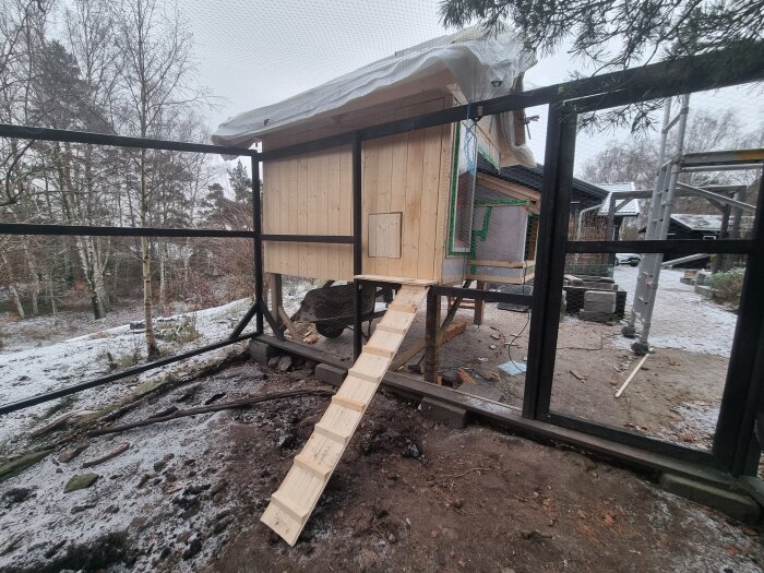 Konstruktion av litet trähus på plattform med metallstommen. Område täckt av snö. Stege av plankor till huset.