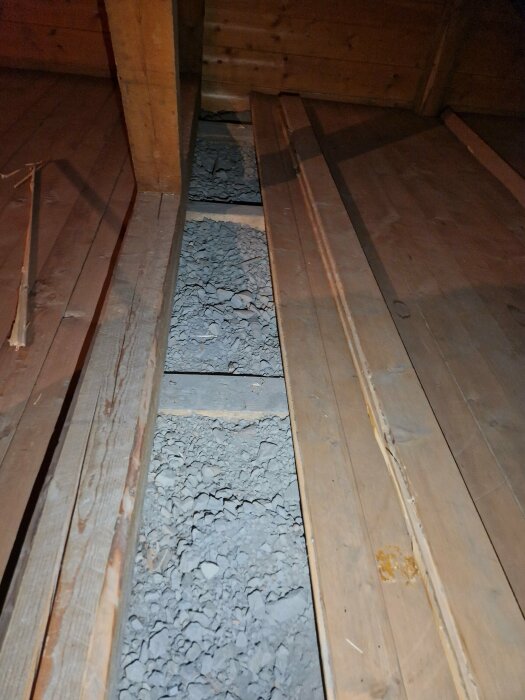 Ett golv av träplankor med en öppning fylld med småstenar, troligen under reparation eller konstruktion.
