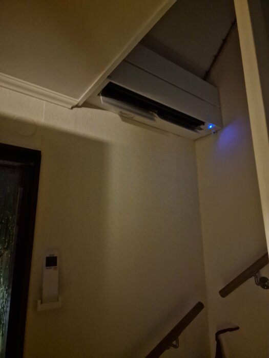 Luftkonditioneringsenhet ovanför trappan, blått ljus, termostat på väggen, mörkt, heminteriör.