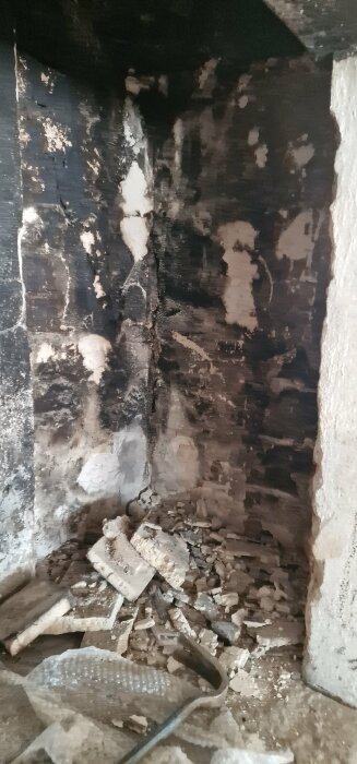 Beskådad ugn med sotiga väggar, aska och rester av brandskador. Verkar föråldrad och oanvänd.