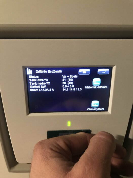 Digital display visar värmesysteminformation, person trycker på knapp, tekniska data presenteras.