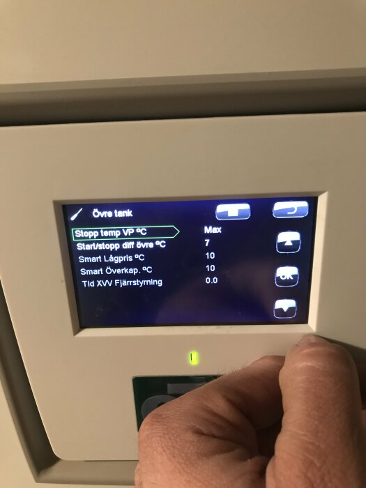 Digital termostat med inställningar visas, hand trycker på knapp, text på svenska, inomhusmiljö.