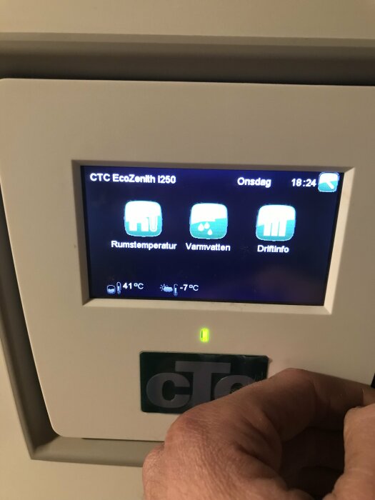 Digital termostatpanel för värmesystem, visar temperatur, tid, och datum med ikoner för rumstemperatur och varmvatten.