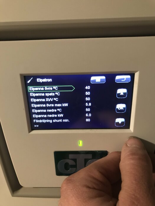 En person justerar inställningar på en digital kontrollpanel för uppvärmningssystem.
