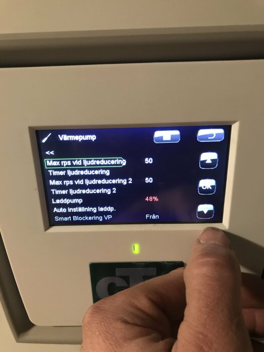 Digital kontrollpanel för värmepump med en hand som trycker på en knapp. Meny med inställningar visas.